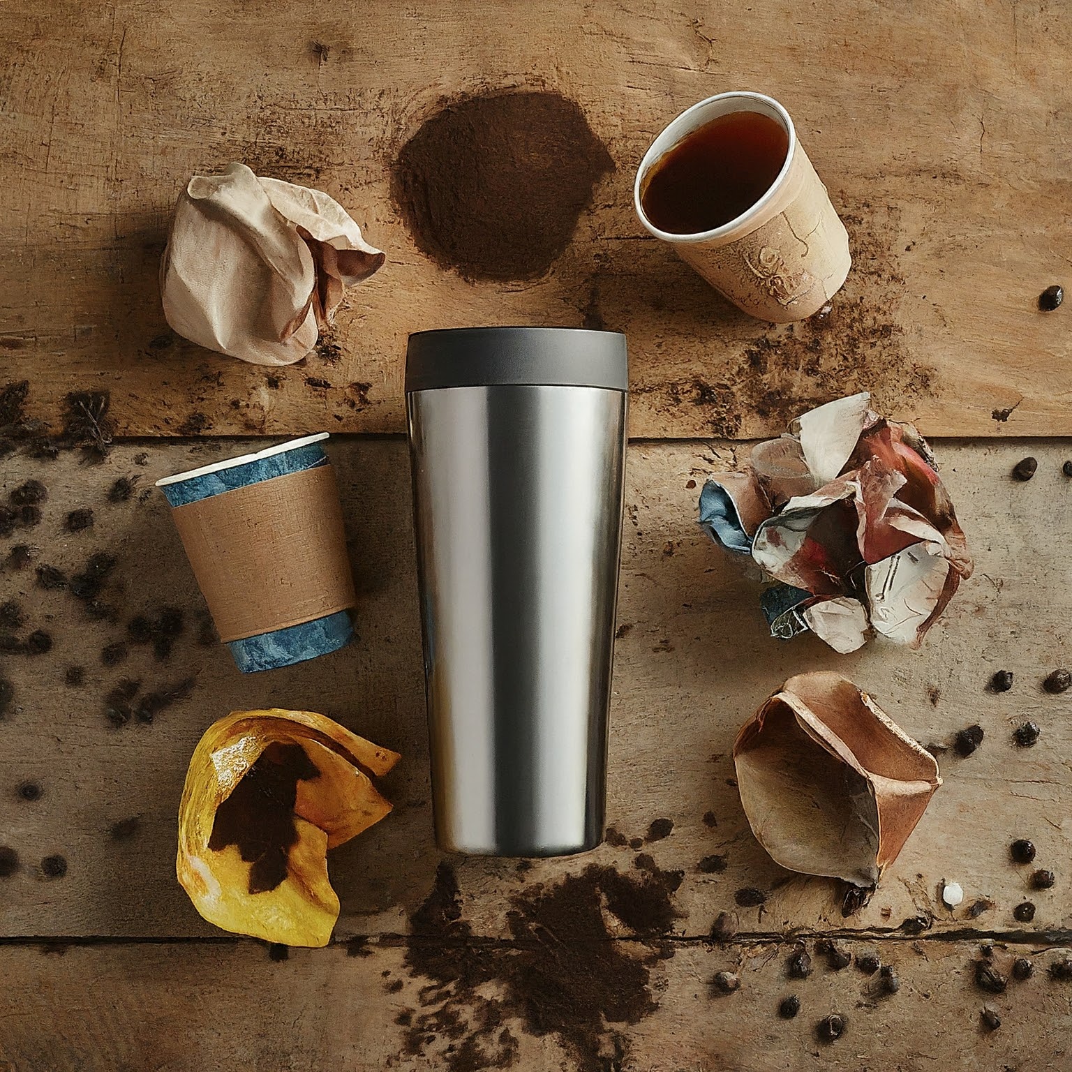 A stainless steel tumbler amidst a scene of used items including crumpled paper cups, soiled napkins, and spilled coffee beans, illustrating the need for sustainable practices in coffee consumption.